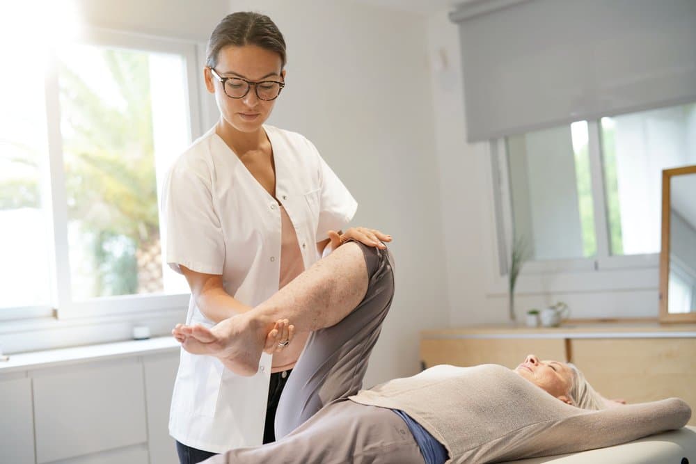 A therapist gently moving a reclining patient's hip and knee through their range of motion.
