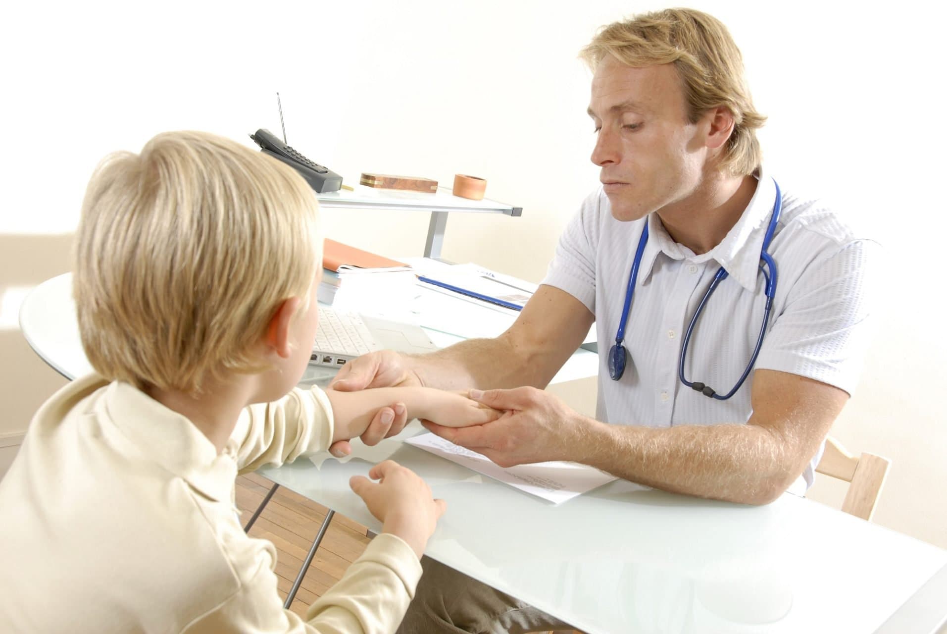 A doctor holding and examining a young patient's wrist.